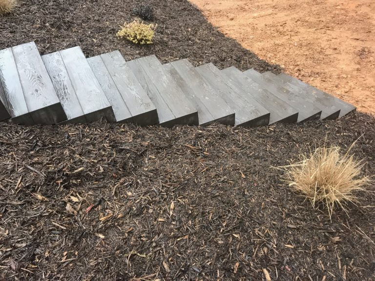 Modern grey outdoor staircase on a dark mulch slope.
