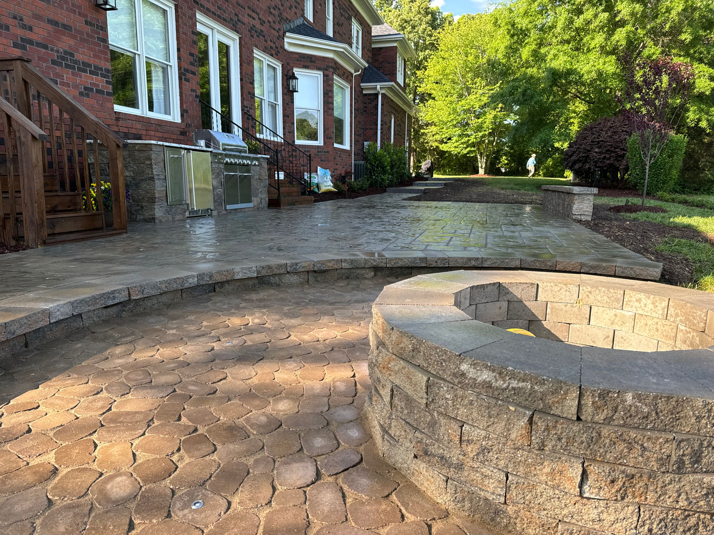 Stone fire pit on a tiered brick patio behind a home.